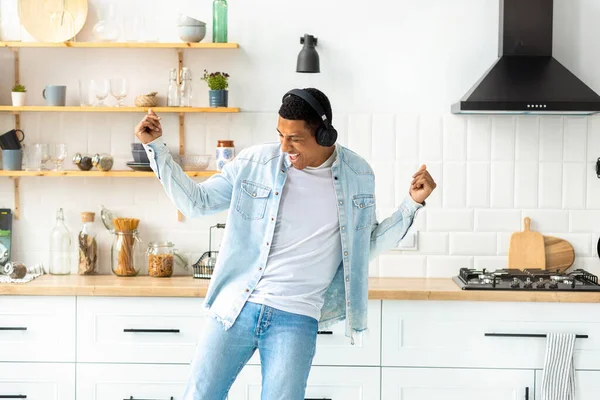 Happy carefree freedom young man in headphones dancing at home in the kitchen alone having fun