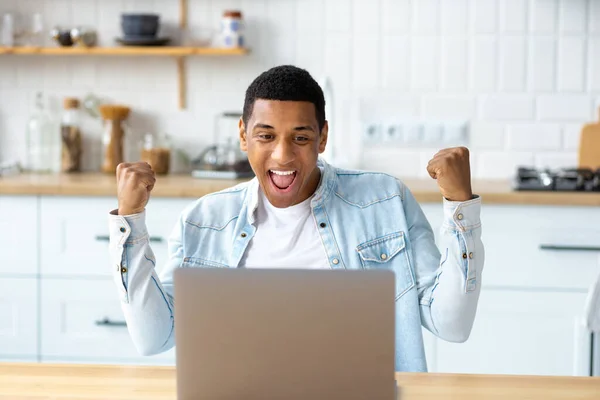 Excited African American man freelancer or student reading good news in email, getting job promotion or scholarship. Overjoyed emotional young male showing yes gesture using laptop celebrating success