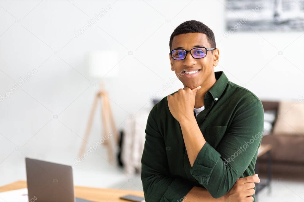 Portrait of successful young african american businessman with eyeglasses standing in modern office. Happy entrepreneur looking at the camera and smiling friendly