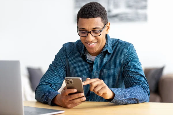 Young African American man entrepreneur in modern office looking at screen typing message with mobile phone. Chatting, social network