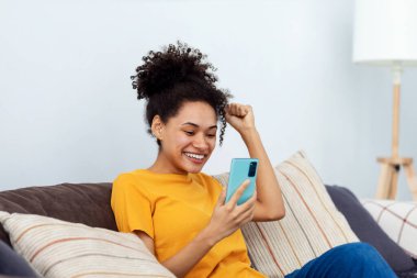 Heyecanlı genç Afrikalı Amerikalı kadın cep telefonundan iyi bir mesaj aldı, harika haberlerle mutlu.