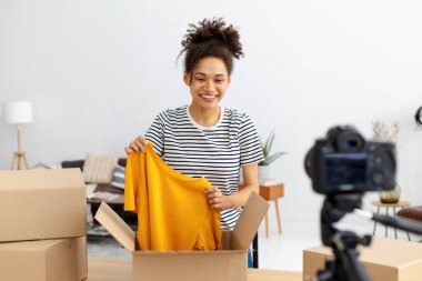 African American female vlogger freelancer using camera to recording video content makes review of products ordered online. Woman owner of online clothing store shoots an advertisement