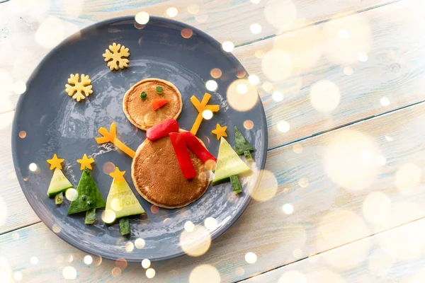Christmas pancake healthy shaped like a snowman with fresh vegetables blue plate on wooden white table decorated festively. Christmas fun food for kids, funny breakfast brunch idea xmas — Stock Photo, Image