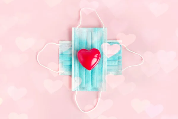 Sevgililer Günü kırmızı kalbi, pembe arka planda tıbbi koruma maskeleri, Coronavirus Valentine. Sağlık hizmetleri kavramı. Sevgililer Günü konsept bakımı.
