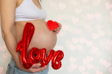 Pregnant belly on Valentines Day with LOVE inflatable balloons and red heart. Love and pregnancy concept, of romance, Valentine Day, Mothers Womans Day.