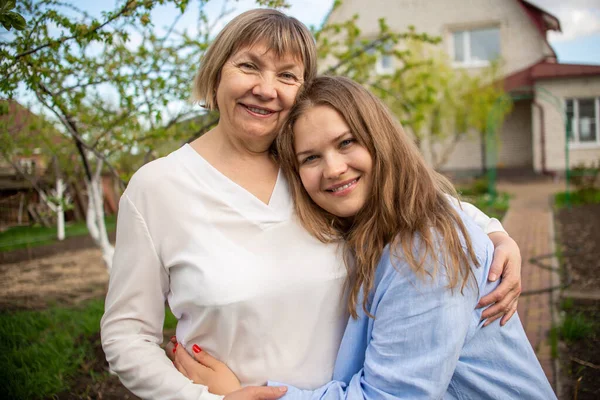Anne ve kızı dışarıda ağaçların ve evin arka planında sarılıyorlar. Anne ve kızı arasındaki ilişki. Aile kavramı ve mutlu aile