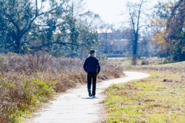 NEW ORLEANS, LA, USA - FEBRUARY 10, 2022: Unidentifiable solitary man with gray hair walks on path in forest