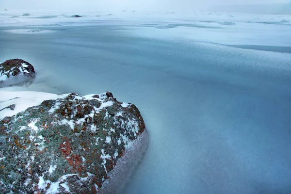 Pierre grise avec des taches rouges sur le rivage d'une baie gelée en hiver — Photo