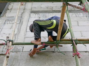 A construction worker working on bamboo scaffolds that are installed around the constructing house - working at height