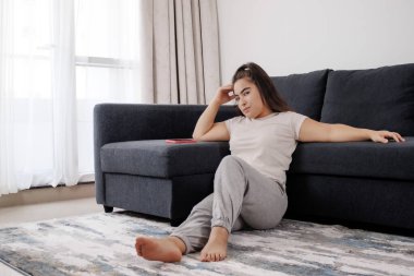 Kanepede oturan ve kameraya bakan genç bir kadın.