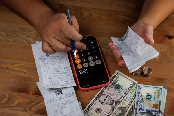 Hesap makinesi, bir fincan kahve ve ahşap bir masada akıllı telefon olan bir adamın elleri.