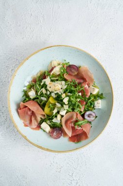 Beyaz tabakta parma jambonlu salata, domates ve roka.