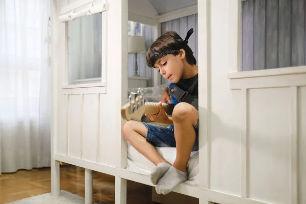 Young musician child with a bandana in his head sitting in his bedroom playing the bass.