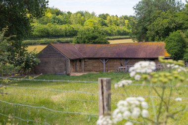 Arkasında ağaçlar olan eski saman ambarı ve önü bulanık çitler.