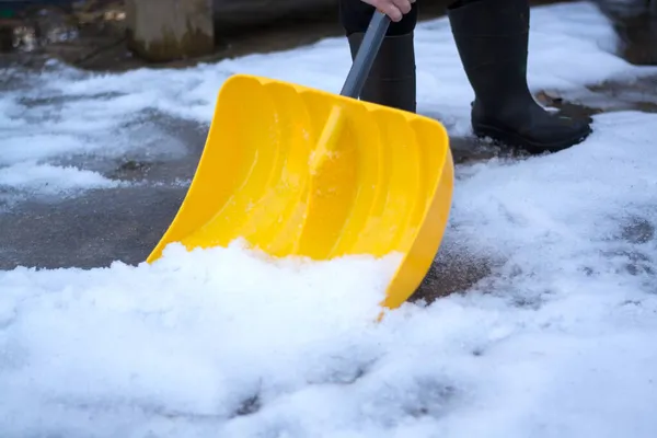 Человек с жёлтой снежной лопатой очищает снег на заднем дворе или во дворе. Зимние работы. — стоковое фото