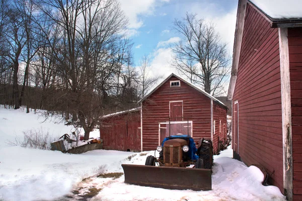 Viejo, abandonado, granero rojo de la vendimia con el viejo tractor oxidado que permanece junto a él. Invierno país escena — Foto de Stock