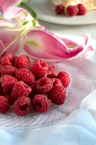 Delicious raspberries on plate with lily flower on background. Antioxidant for healthy living — Stock Photo, Image