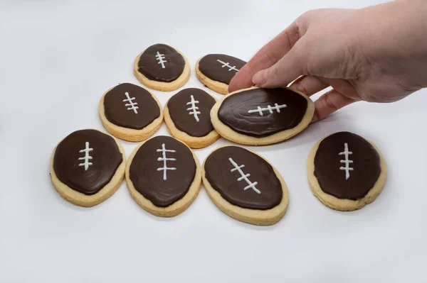 Football shape cookies. Hand taking cookie. Home made cookies concept. Super Bowl party cookies. High quality photo