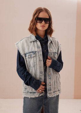 Kendine güvenen genç bir kadının moda portresi, manken, kot ceket ve etek giyiyor. Güneş gözlüğü takan kadın. Kot gömlekli güzel bir kadın. Kot pantolon gibi görünüyor. Stüdyo resmi