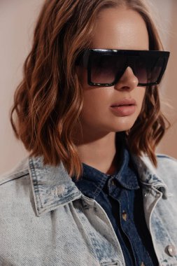 Moda gözlükleri takan genç ve güzel bir kadın. Yakın çekim stüdyo portresi. Kısa kıvırcık saçlı bayan. Kot ceket giyen bir model. moda yakın plan portresi