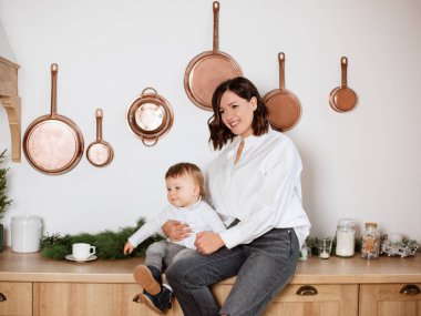 Oğluyla mutlu bir anne. Mutfakta gülümseyen anne. Güzel bir aile portresi. 1 yaşındaki bebeğini kucağında tutan kadın.