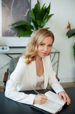 İlham arıyorum. Genç, güzel, gülümseyen bir kadın bazı notlar alıyor ve çalışma yerinde sandalyede otururken kameraya bakıyor.