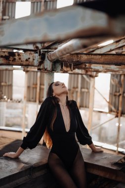 Siyah elbiseli ve metal endüstriyel merdivenlerde poz veren gümüş çizmeli cesur bir kadının portresi. Şehirli grunge stili. Kadın modası..