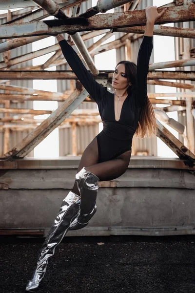 Portrait of a handsome courageous woman in black clothes and silver boots posing on a metal industrial staircase. Urban grunge style. Female fashion.