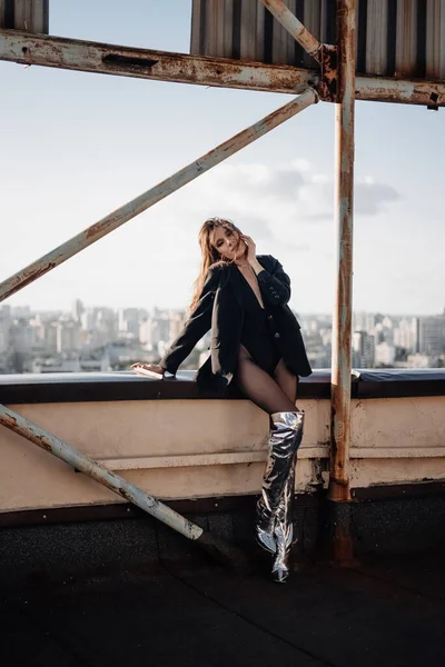 fashion model posing on rooftop. city view. beautiful woman wearing silver boots. fashion concept