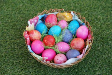 Doğa yeşili çimen arka planında renkli paskalya yumurtalarının olduğu sepet. Paskalya tatili konsepti. Bahçede boyanmış paskalya yumurtaları. Hasır sepette ev yapımı paskalya yumurtası koleksiyonu.