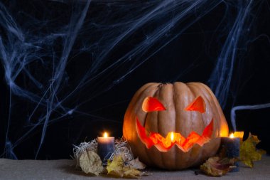 Balkabağı 'nın stüdyo fotoğrafı, yanan mumlar ve karanlık arka planda örümcek ağı. Cadılar Bayramı kavramsal fotoğrafı. Metin için boşluk