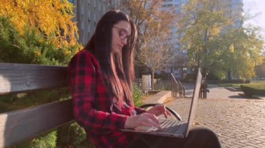 Ciddi, güzel, genç bir kadın dışarıda dizüstü bilgisayarla oturmuş internet üzerinden iletişim teknolojisi yazıyor.