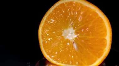 Stüdyoda çekilen su damlaları, kesilmiş portakal meyvelerinin üzerine düşer. Siyah arka plan. 4K video görüntüleri