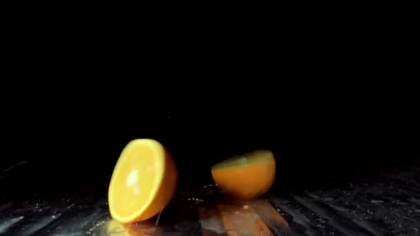Orangene Früchte fallen auf den Tisch und werden auf schwarzem Hintergrund in zwei Hälften unterteilt — Stockvideo