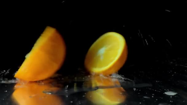 Pomerančové ovoce padající na stůl a rozdělené na dvě poloviny na černém pozadí
