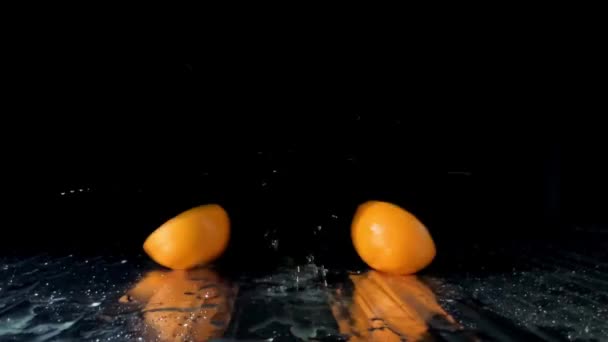 Orange fruit falling on table and divided into two halves on black background — Stock Video