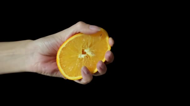 Vrouwelijke hand knijpt sinaasappel fruit geïsoleerd op zwarte achtergrond. — Stockvideo