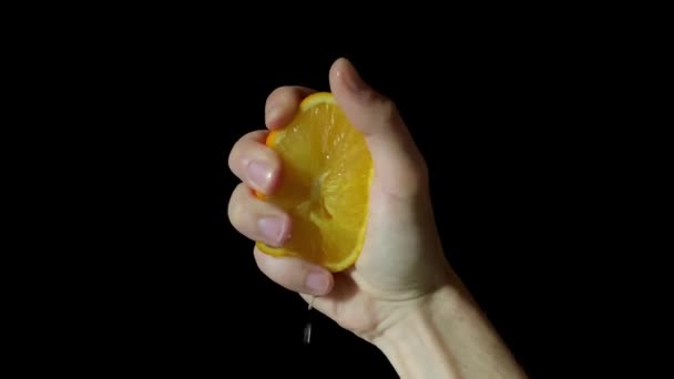 Чоловіча рука стискає шматочок соковитого апельсина на чорному фоні в студії, крупним планом — стокове відео