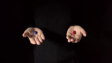 Karar verme kavramı. Kırmızı hap ya da mavi hap öneriyor. İnsan eli kırmızı ve mavi hapları tutar. Karanlık arka plan. Stüdyo 4K görüntüsü