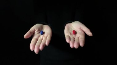 Karar verme kavramı. Kırmızı hap ya da mavi hap öneriyor. İnsan eli kırmızı ve mavi hapları tutar. Karanlık arka plan. Stüdyo 4K görüntüsü
