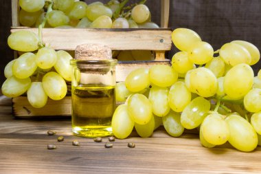 Küçük şarap şişesinde üzüm yağı tohumu. Yeşil dilimli bir yığın üzüm tohumu ve organik yağ, tentür, özü, ahşap kırsal arkaplan üzerine aşılama.