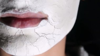 Kadının yüzüne kilden maske yakın çekim, arka planda stüdyo resmi.