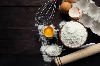 Hamur işleri için malzemeler: un, yumurta, koyu ahşap arka planda yumurta sarısı. Düz yatıyordu. Üst görünüm.