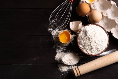 Hamur işleri için malzemeler: un, koyu ahşap arka planda yumurtalar. Mesaj için yer var. Üst görünüm.