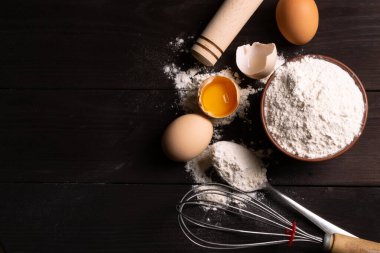 Hamur işleri için malzemeler: un, koyu ahşap arka planda yumurtalar. Mesaj için yer var. Üst görünüm.