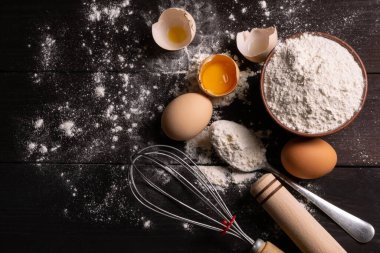 Pişirmek için gerekli malzemeler. Yumurta sarısı, un ve hamur çırpmak için çırpılmış çırpılmış tavuk yumurtası ve koyu ahşap arka planda hamur karıştırıcı. Düz yatıyordu. Fırın kavramı