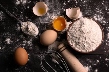 Pişirmek için gerekli malzemeler. Yumurta sarısı, un ve hamur çırpmak için çırpılmış çırpılmış tavuk yumurtası ve koyu ahşap arka planda hamur karıştırıcı. Düz yatıyordu. Fırın kavramı