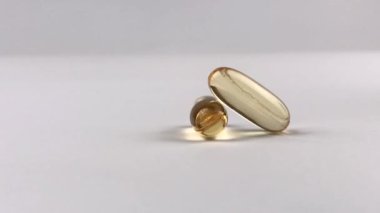 Beyaz arka planda balık yağı olan iki sarı hap. Omega-3 altın hapları. Kapsüllere yakın çekim. İlaç sanayisi. 4K, UHD