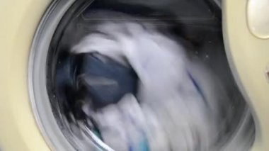 Beyaz çamaşır makinesi kirli beyaz ve renkli giysileri yıkar. Çamaşır makinesinde çamaşır yıkamak. Dönen davul çamaşır makinesinin videosunu kapat.
