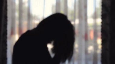 Pencerenin yanındaki depresyondaki genç bir kadının dikkatsiz silueti. Bulanık arkaplan